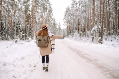 Kış ormanında güzel genç bir kadın araba bekliyor. Kışın otostop yapmak. Harika bir kar günü. Araba yolculuğu kavramı.