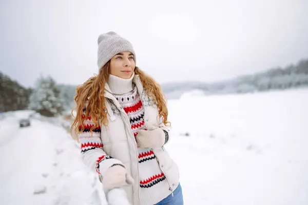 Beautiful young woman in winter clothes enjoying the winter forest. Behind her is a snow-covered lake. Happy winter time. Christmas.