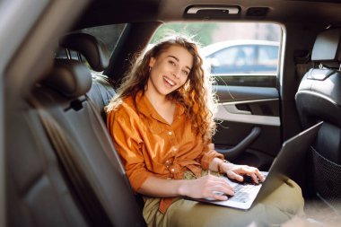 Güzel bir iş kadını bir arabanın arka koltuğunda otururken dizüstü bilgisayar kullanıyor. Arabada dizüstü bilgisayarla çalışan serbest çalışan genç bir kadın. Serbest, ulaşım kavramı.