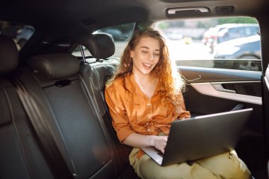 Güzel bir iş kadını bir arabanın arka koltuğunda otururken dizüstü bilgisayar kullanıyor. Arabada dizüstü bilgisayarla çalışan serbest çalışan genç bir kadın. Serbest, ulaşım kavramı.