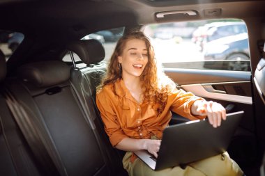 Güzel bir iş kadını bir arabanın arka koltuğunda otururken dizüstü bilgisayar kullanıyor. Arabada dizüstü bilgisayarla çalışan serbest çalışan genç bir kadın. Serbest, ulaşım kavramı.