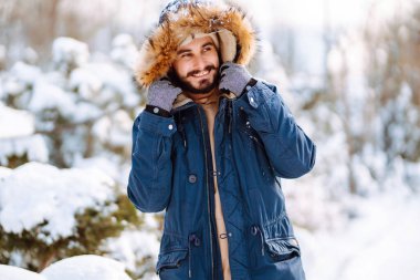 Genç sakallı bir adam karlı bir parkta yürüyor. Mutlu adam güneşli bir kış gününde havanın tadını çıkarıyor. Yürüyüş kavramı, hafta sonları.