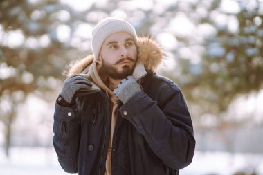 Genç sakallı bir adam karlı bir parkta yürüyor. Mutlu adam güneşli bir kış gününde havanın tadını çıkarıyor. Yürüyüş kavramı, hafta sonları.