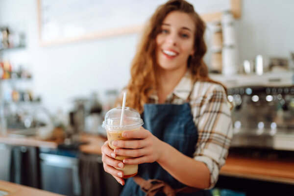 Portrait of a smiling female barista with a takeaway drink standing behind a bar counter. Business concept, food and drinks.
