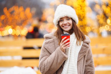 Gülümseyen kadın Noel ışıklarıyla süslenmiş bir Noel pazarında yürüyor. Genç bir kadın açık havanın tadını çıkarıyor. Tatil kavramı, rahatlama..