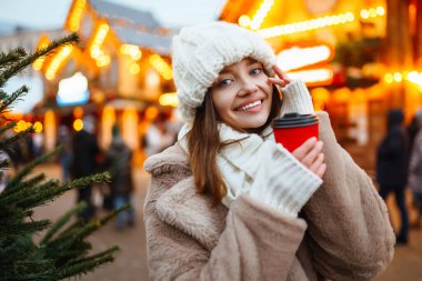 Gülümseyen kadın Noel ışıklarıyla süslenmiş bir Noel pazarında yürüyor. Genç bir kadın açık havanın tadını çıkarıyor. Tatil kavramı, rahatlama..