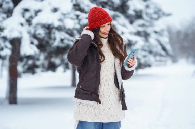 Parkta telefonuyla yürüyen, selfie çeken, blog yazan mutlu bir kadın. Genç bayan turist karlı bir parkta eğleniyor. Doğa kavramı, eğlence, rahatlama.