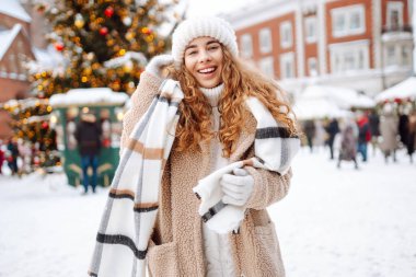 Eşarplı ve şapkalı gülümseyen kadın, bir panayırda eğleniyor, sıcak bir içki içiyor. Noel konsepti, kış tatili. Yaşam biçimi.