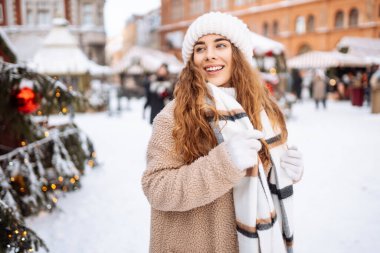 Eşarplı ve şapkalı gülümseyen kadın, bir panayırda eğleniyor, sıcak bir içki içiyor. Noel konsepti, kış tatili. Yaşam biçimi.