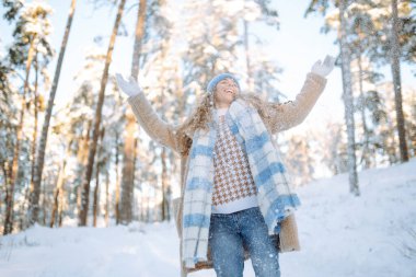 Kar yağışlı kış gününde eşarp ve şapka takan mutlu kadın. Genç bir kadın soğuk bir günde karla eğleniyor. Yürüme konsepti.