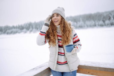 Tatlı bir kadın, karlı bir ormanda termostan sıcak bir içecek içer. Kış yürüyüşü. Genç bayan turist dışarıda havanın tadını çıkarıyor..