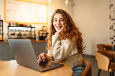 Genç bir kadın bir kafede otururken dizüstü bilgisayarla çalışıyor. Freelancer, modern bir kafede online olarak çalışıyor. Teknoloji kavramı, serbest çalışma. Yaşam biçimi.