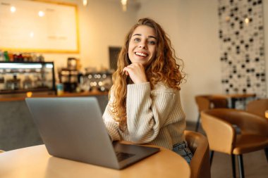 Genç bir kadın bir kafede otururken dizüstü bilgisayarla çalışıyor. Freelancer, modern bir kafede online olarak çalışıyor. Teknoloji kavramı, serbest çalışma. Yaşam biçimi.