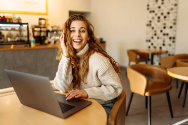 Genç bir kadın bir kafede otururken dizüstü bilgisayarla çalışıyor. Freelancer, modern bir kafede online olarak çalışıyor. Teknoloji kavramı, serbest çalışma. Yaşam biçimi.