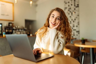 Genç bir kadın bir kafede otururken dizüstü bilgisayarla çalışıyor. Freelancer, modern bir kafede online olarak çalışıyor. Teknoloji kavramı, serbest çalışma. Yaşam biçimi.