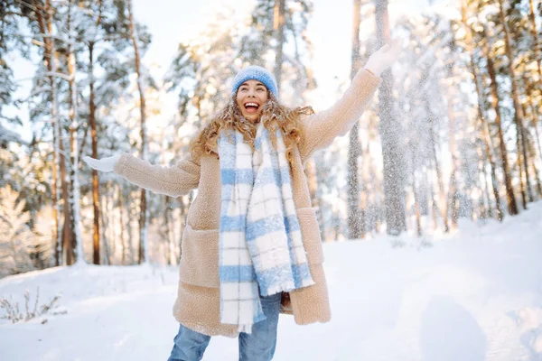Happy woman wearing scarf and hat on snowy winter day outdoors. Young woman having fun with snow on a frosty day. Walking concept.