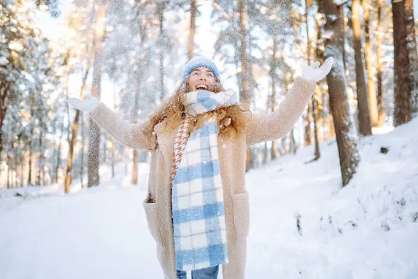 Happy woman wearing scarf and hat on snowy winter day outdoors. Young woman having fun with snow on a frosty day. Walking concept.