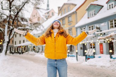 Parlak ceketli gülümseyen kadın karlı bir caddede karla eğleniyor. Genç bir kadın açık havada karlı havanın tadını çıkarıyor. Rahatlama kavramı, eğlence. Yaşam biçimi.