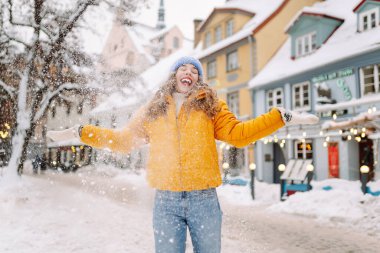 Parlak ceketli gülümseyen kadın karlı bir caddede karla eğleniyor. Genç bir kadın açık havada karlı havanın tadını çıkarıyor. Rahatlama kavramı, eğlence. Yaşam biçimi.