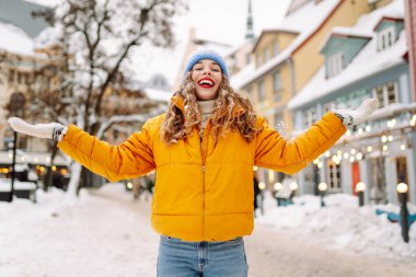 Parlak ceketli gülümseyen kadın karlı bir caddede karla eğleniyor. Genç bir kadın açık havada karlı havanın tadını çıkarıyor. Rahatlama kavramı, eğlence. Yaşam biçimi.