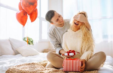Yatak odasında balonlarla süslenmiş, birlikte eğlenen genç ve güzel bir çift. Bir erkek ve bir kadın tatillerini evde yatakta kutluyorlar. İlişki kavramı, tatil.