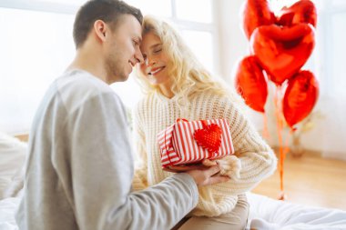 Yatak odasında balonlarla süslenmiş, birlikte eğlenen genç ve güzel bir çift. Bir erkek ve bir kadın tatillerini evde yatakta kutluyorlar. İlişki kavramı, tatil.