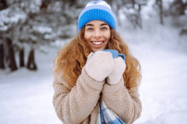 Karlı bir ormanda termosla gülen bir kadın doğanın tadını çıkarıyor. Dışarıda sıcak bir şeyler içen genç bir kadın. Macera konsepti. Yaşam biçimi.