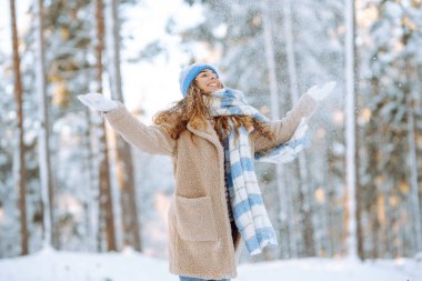 Sıcak elbiseli genç bir kadın güneşli bir kış gününde karla oynar. Mutlu bayan turist parkta karlı bir günün tadını çıkarıyor. Yürüme kavramı, eğlence.