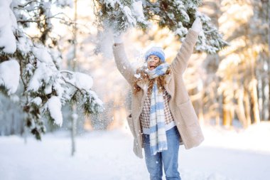 Sıcak elbiseli genç bir kadın güneşli bir kış gününde karla oynar. Mutlu bayan turist parkta karlı bir günün tadını çıkarıyor. Yürüme kavramı, eğlence.