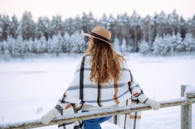 Kar ormanında şapkalı ve atkılı gülümseyen bir kadının portresi kış gününün tadını çıkarıyor. Genç gezgin dışarıda poz veriyor. Macera, hafta sonu konsepti.