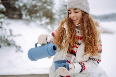 Güzel genç bir kadın termosla çay içer. Harika kış havası, karlı göl. Kış yürüyüşü. Genç bayan turist dışarıda havanın tadını çıkarıyor..
