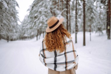Güzel bir kadın kış ormanında sırt üstü poz veriyor. Harika bir kış havası ve atmosfer. O, kışlık bir ceket, şapka ve eşarp giydi. Kış tatilin kutlu olsun. Noel.