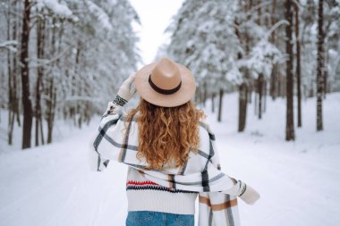 Güzel bir kadın kış ormanında sırt üstü poz veriyor. Harika bir kış havası ve atmosfer. O, kışlık bir ceket, şapka ve eşarp giydi. Kış tatilin kutlu olsun. Noel.