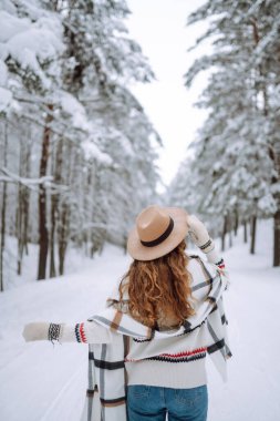 Güzel bir kadın kış ormanında sırt üstü poz veriyor. Harika bir kış havası ve atmosfer. O, kışlık bir ceket, şapka ve eşarp giydi. Kış tatilin kutlu olsun. Noel.