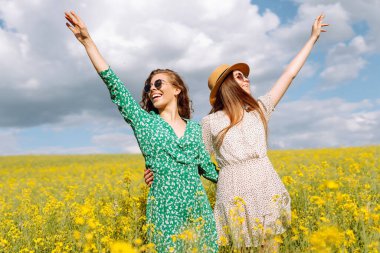 Sarı kolza tohumu tarlasının ortasında mutlu iki genç kadın. Kız arkadaşlar güneşli bir günde dışarıda eğleniyorlar. Eğlence anlayışı, rahatlama. Yaşam biçimi.