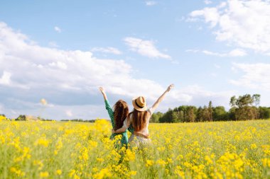 Sarı kolza tohumu tarlasının ortasında mutlu iki genç kadın. Kız arkadaşlar güneşli bir günde dışarıda eğleniyorlar. Eğlence anlayışı, rahatlama. Yaşam biçimi.