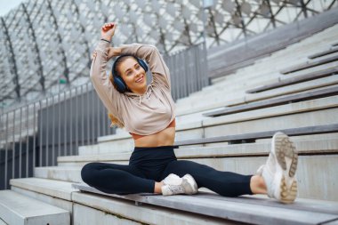 Havalı spor kıyafetleriyle spor yapan kadın dışarıda spor yapıyor. Genç bir kadın egzersiz yapıyor, esneme egzersizleri yapıyor. Aktif yaşam tarzı konsepti, spor.