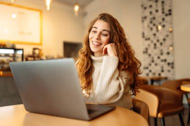 Happy woman working with laptop in cafe. A young woman freelancer in a modern coffee shop is working on a laptop. Technology concept, freelancing. Lifestyle.