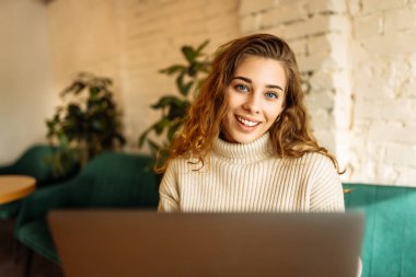 Happy woman working with laptop in cafe. A young woman freelancer in a modern coffee shop is working on a laptop. Technology concept, freelancing. Lifestyle.
