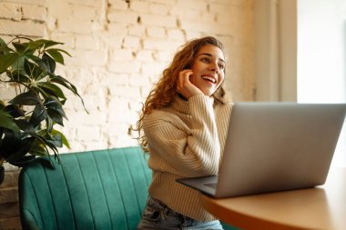 Happy woman working with laptop in cafe. A young woman freelancer in a modern coffee shop is working on a laptop. Technology concept, freelancing. Lifestyle.