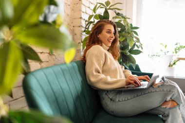 Happy woman working with laptop in cafe. A young woman freelancer in a modern coffee shop is working on a laptop. Technology concept, freelancing. Lifestyle.