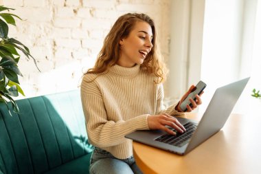 Happy woman working with laptop in cafe. A young woman freelancer in a modern coffee shop is working on a laptop. Technology concept, freelancing. Lifestyle.