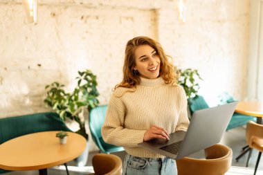 Happy woman working with laptop in cafe. A young woman freelancer in a modern coffee shop is working on a laptop. Technology concept, freelancing. Lifestyle.