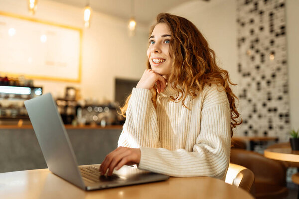 Happy woman working with laptop in cafe. A young woman freelancer in a modern coffee shop is working on a laptop. Technology concept, freelancing. Lifestyle.