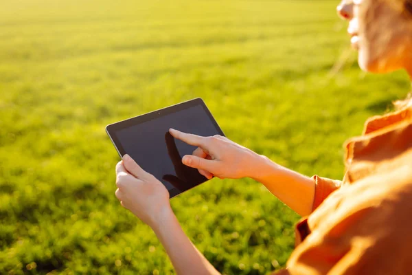Smart agriculture. A young woman farmer wearing glasses holds a tablet on a green wheat field. A woman agronomist checks the quality of the crop using a digital tablet. Agriculture concept.