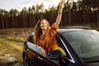 Arabasının camından sarkıp seyahatin tadını çıkaran genç ve mutlu bir kadın. Aktif yaşam tarzı, seyahat, turizm, doğa.