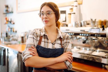 Modern bir kafe barında önlüklü güzel bir baristanın portresi. Küçük işletme sahibi başarılı bir kadın kafe restoranında duruyor. İş konsepti.