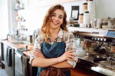 Modern bir kafe barında önlüklü güzel bir baristanın portresi. Küçük işletme sahibi başarılı bir kadın kafe restoranında duruyor. İş konsepti.