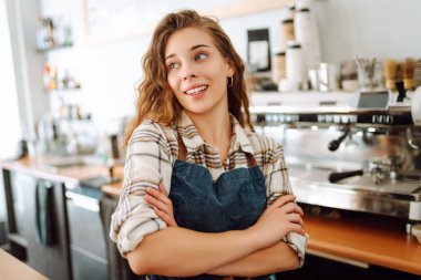 Modern bir kafe barında önlüklü güzel bir baristanın portresi. Küçük işletme sahibi başarılı bir kadın kafe restoranında duruyor. İş konsepti.