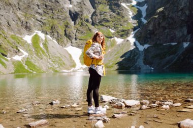 Sırt çantasıyla dağlarda gezen genç bir kadın. Sportif genç kadınlarla manzara, tepeler, orman, gökyüzü. Seyahat ve turizm. Yürüyüş.